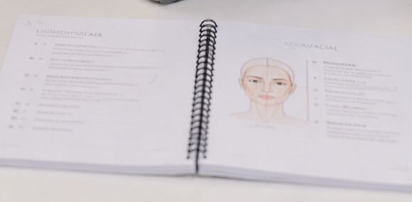 Aufgeschlagene Schulungsunterlagen mit Gesichtsschema aus dem Aquafacial-Training.